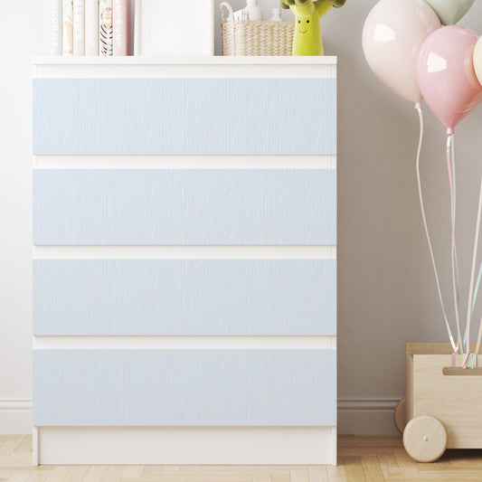 Vit IKEA MALM-byrå med fyra lådor klädda i ljusblå dekorfolie med tunna vita, vågiga linjer i ett barnrum.
