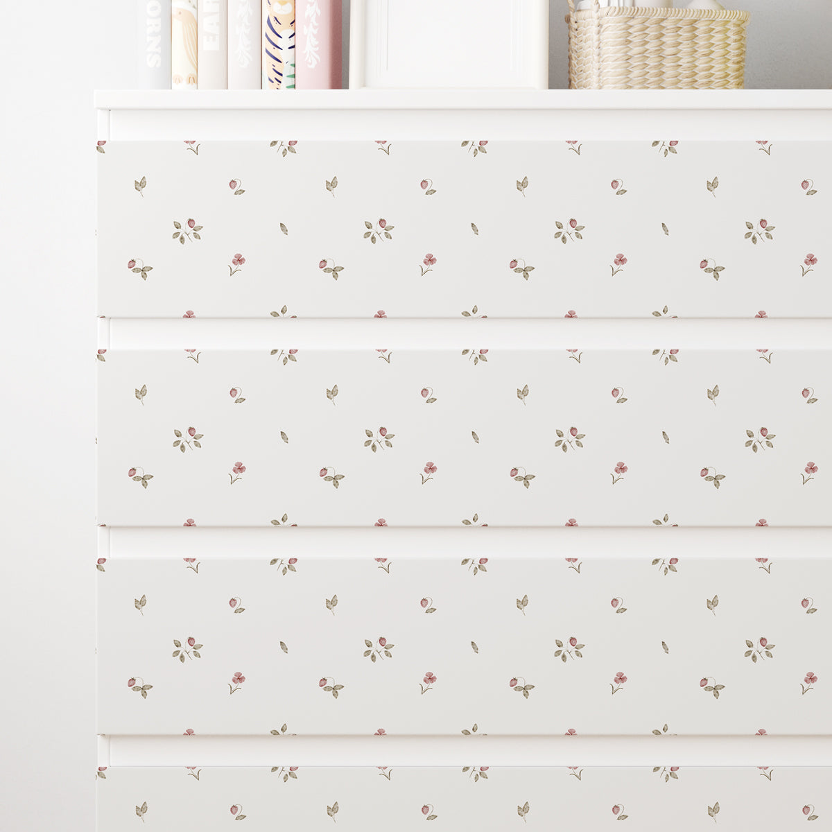 Närbild av en vit IKEA MALM-byrå med dekorfolie med små rosa jordgubbar, gröna blad och nätta blommor.
