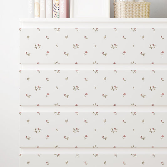 Närbild av en vit IKEA MALM-byrå med dekorfolie med små rosa jordgubbar, gröna blad och nätta blommor.
